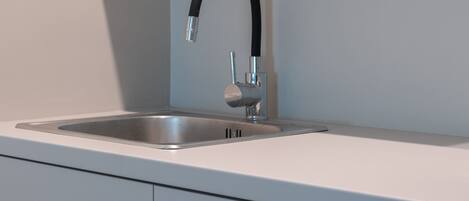 Eine moderne Küche mit Spüle aus Edelstahl, einem gebogenen Wasserhahn und einer weißen Arbeitsplatte.