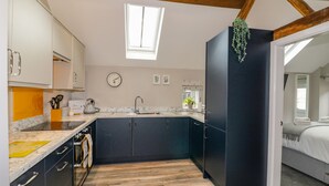 A compact kitchen with dark cabinets, a marble countertop, and a wooden ceiling. - The Stables (Stoke-on-Trent)