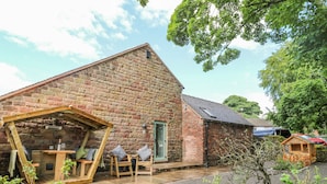 A rustic stone building with a wooden pergola and seating area. - The Stables (Stoke-on-Trent)