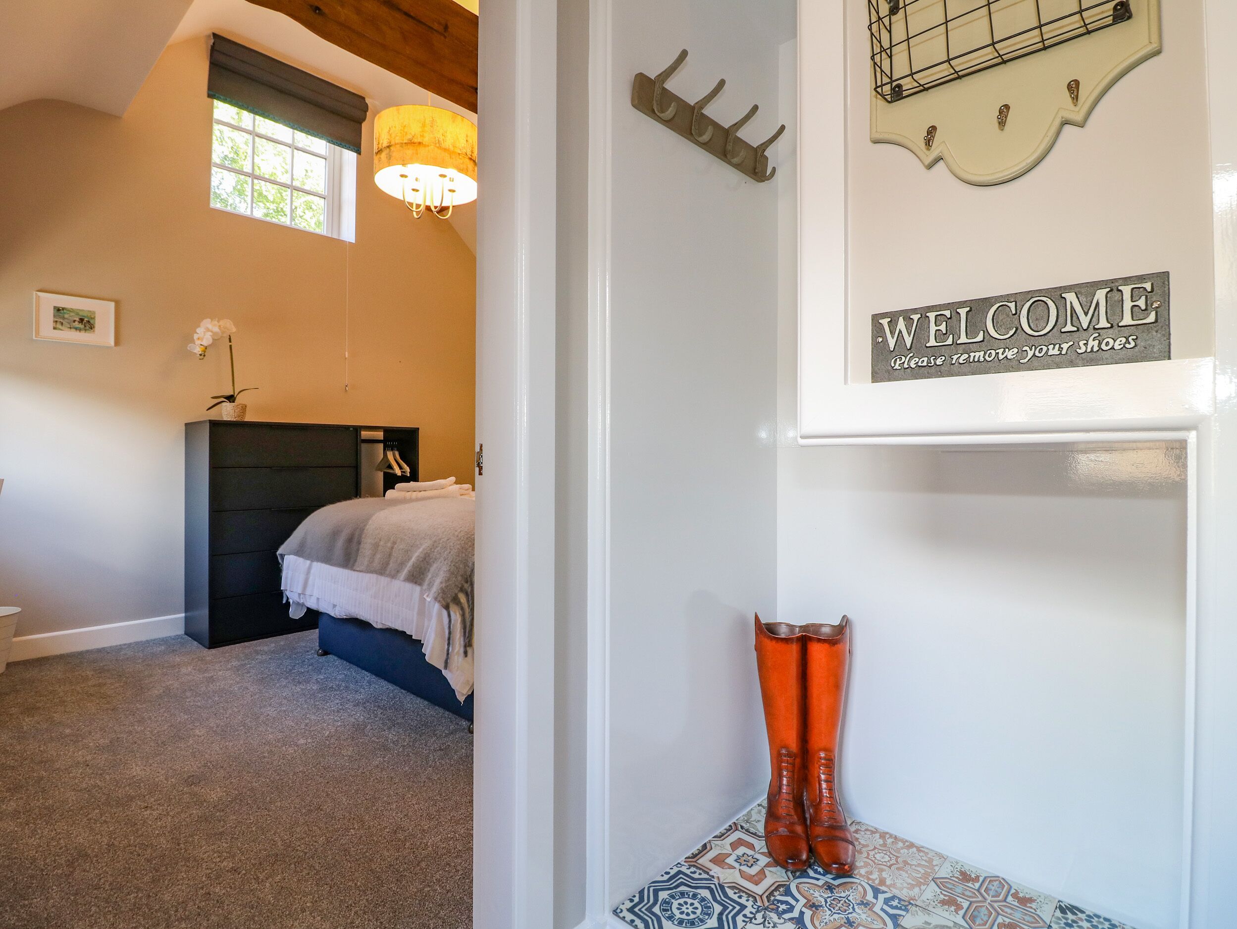 A bedroom with a bed, a nightstand, a lamp, and a 'WELCOME Please remove your shoes' sign.
