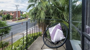 Un balcon avec une chaise et une table, donnant sur une rue animée où l’on peut voir des voitures et des immeubles.