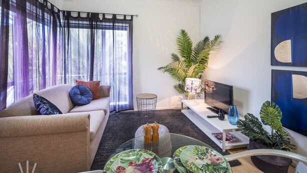 Un salon moderne avec un canapé, une table basse et un téléviseur. On y trouve des coussins décoratifs, une plante et un tapis.
