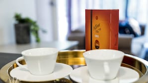 Un plateau avec deux tasses et sous-tasses blanches, une boîte de café Cittadella Oro et un arrière-plan flou avec une plante.