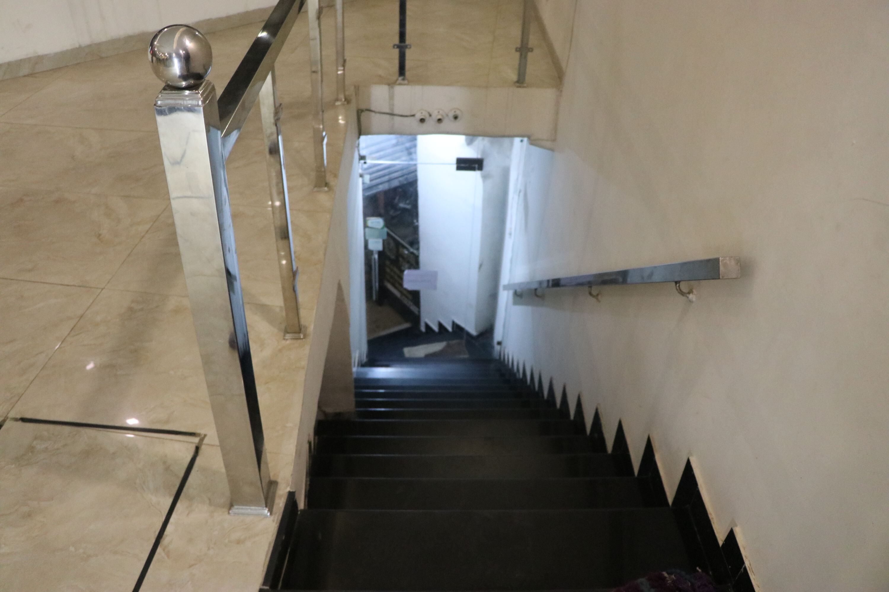 A staircase with a metal handrail and a ball finial, leading to a room with a white wall and a visible door.
