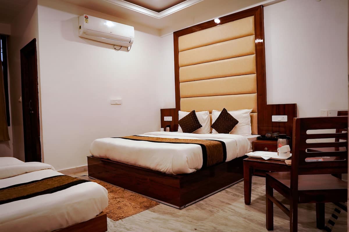 A hotel room with a large bed, a bedside table, a chair, and an air conditioning unit.