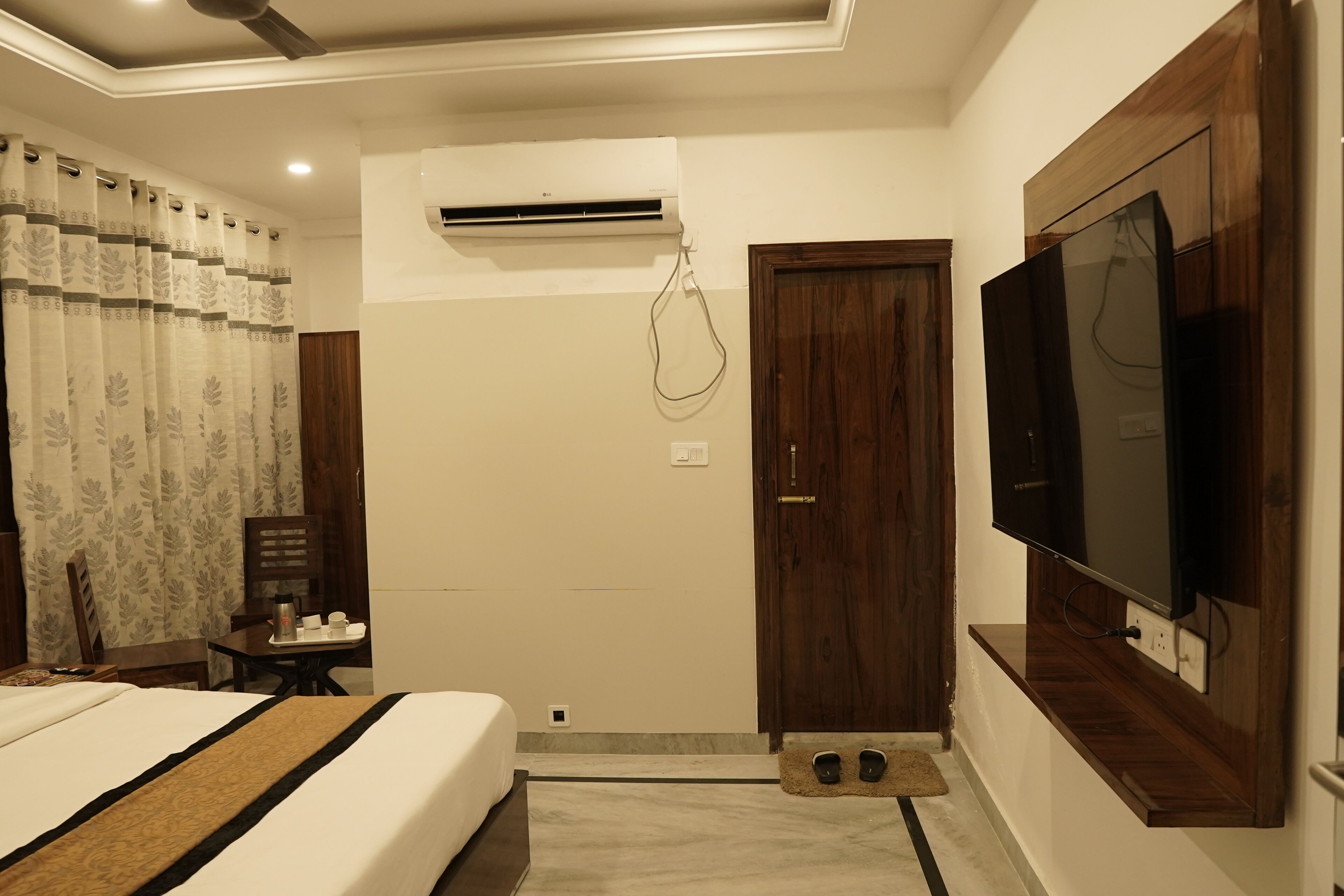 Une chambre d’hôtel avec un lit, un téléviseur fixé au mur, un appareil de climatisation, une porte en bois et une petite table avec une chaise.