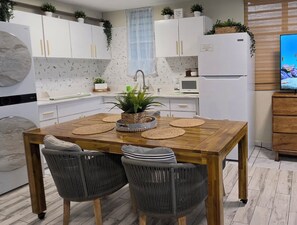 A modern kitchen with white cabinets, a wooden dining table, wicker chairs, and a built-in refrigerator. - Guest Favorite • “True Oceanfront” Luquillo Condo • Walk to Kioskos & El Yunque (Playa Fortuna)