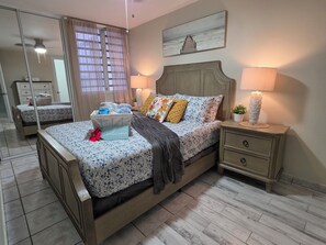 A bedroom with a bed, bedside tables, a nightstand, a mirror, and a window with curtains. - Guest Favorite • “True Oceanfront” Luquillo Condo • Walk to Kioskos & El Yunque (Playa Fortuna)