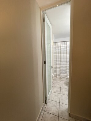 A hallway leading to a bathroom with a shower curtain and tiled floor. - Guest Favorite • “True Oceanfront” Luquillo Condo • Walk to Kioskos & El Yunque (Playa Fortuna)