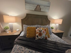 A bedroom with a bed, two bedside tables, a nightstand, a wall-mounted painting, and a potted plant. - Guest Favorite • “True Oceanfront” Luquillo Condo • Walk to Kioskos & El Yunque (Playa Fortuna)
