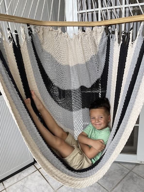 A person lying in a hammock with a striped fabric. - Guest Favorite • “True Oceanfront” Luquillo Condo • Walk to Kioskos & El Yunque (Playa Fortuna)