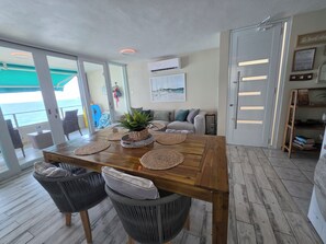 A dining area with a wooden table, woven placemats, and wicker chairs. - Guest Favorite • “True Oceanfront” Luquillo Condo • Walk to Kioskos & El Yunque (Playa Fortuna)