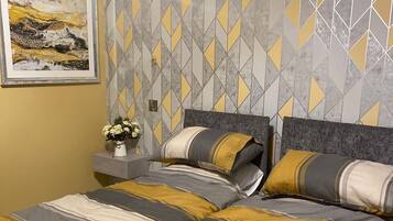 A bedroom with a geometric patterned wallpaper, a framed artwork on the wall, and a bedside table with a vase of flowers.