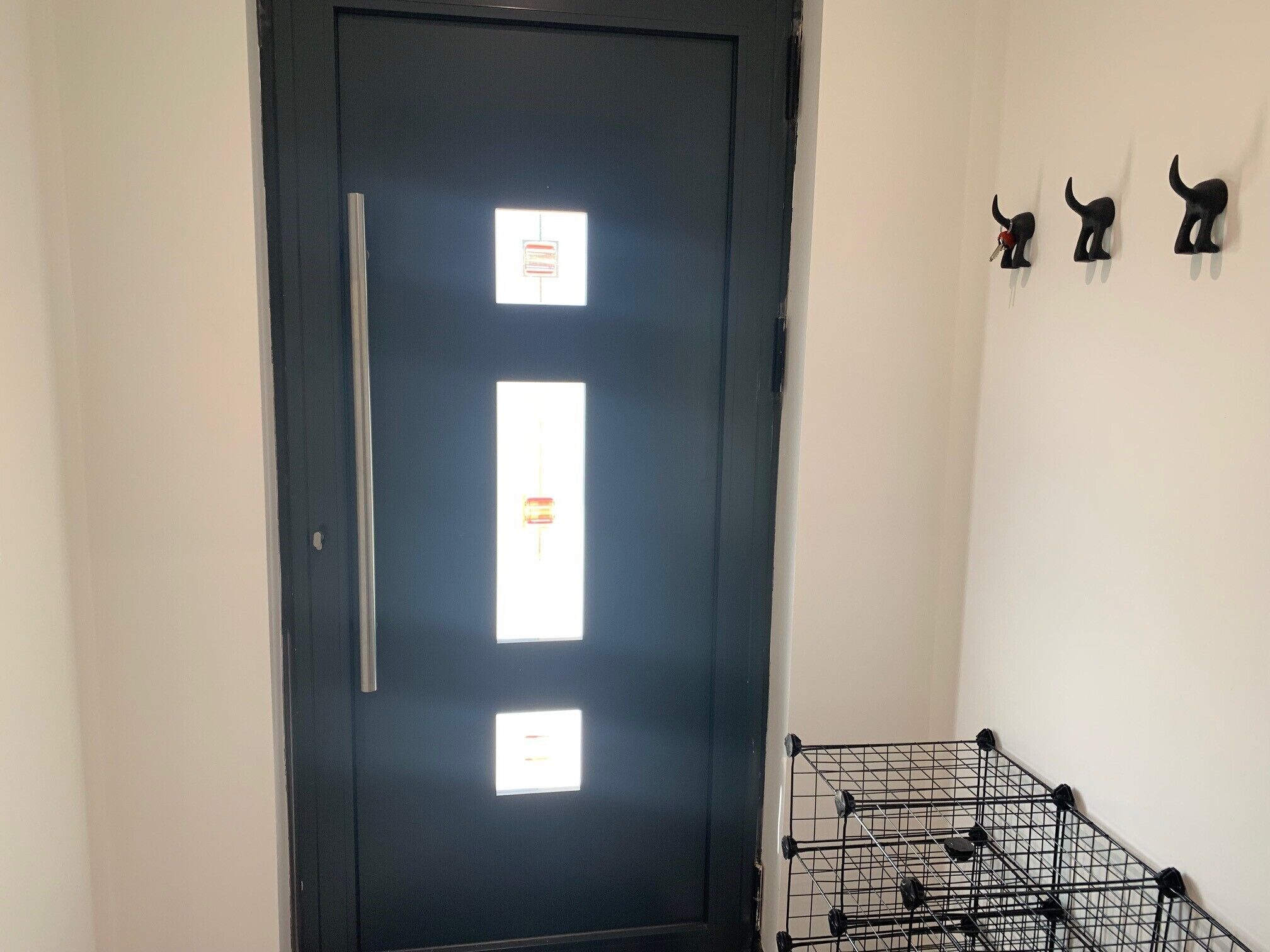 A door with three illuminated panels, a metal rack with keys, and three black cat-shaped wall decorations.