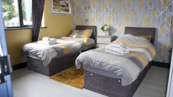 Une chambre d’hôtel avec deux lits, une petite table de chevet ornée d’un vase de fleurs et une fenêtre avec des rideaux.