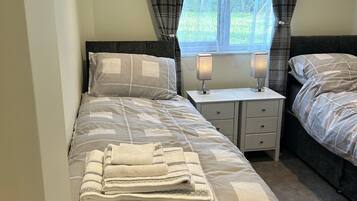 Un dormitorio con dos camas, una ventana con cortinas, una mesita de noche con lámpara y un adorno en la pared.