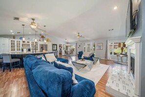 A spacious living area with a blue sofa, a coffee table, and a kitchen in the background. - The Bayou House - Lakefront, Boat Dock, Views! (Hot Springs)