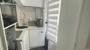 Una cocina compacta con armarios blancos, encimera negra y una cafetera.