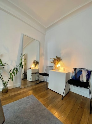 Ein modernes Wohnzimmer mit Holzboden, einem grauen Teppich, einem weißen Sofa, einem schwarzen Sessel und einem großen Spiegel an der Wand.