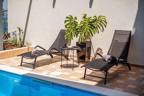 A poolside area with lounge chairs, a small table, and potted plants. - Aigli Luxury Villa - Panoramic Seaview Retreat (Kalamata)