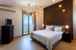 Ein modernes Schlafzimmer mit Bett, Nachttischen, einem Fernseher und einer Glastür zum Balkon.