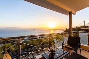 Un balcon doté d’une balustrade en verre offrant une vue imprenable sur le coucher de soleil et la mer.