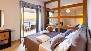 A modern hotel room with a large bed, a balcony with a view, and a sliding door leading to an outdoor area.