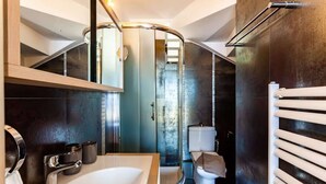 A modern bathroom with a curved mirror, a white sink, a toilet, and a towel rack.