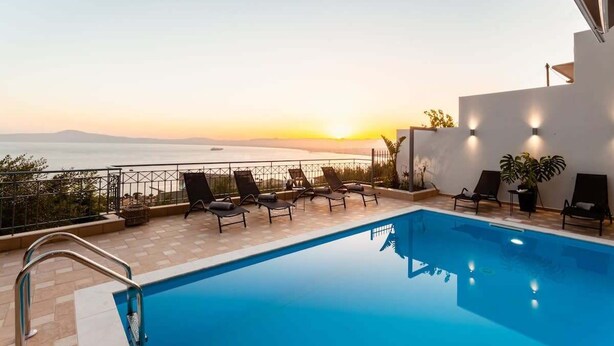 A pool area with lounge chairs and a view of the sunset over the sea.
