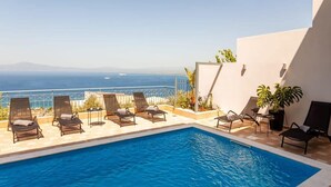 A pool area with lounge chairs and a view of the ocean.