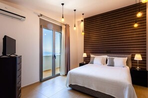 Une chambre d’hôtel comprenant un lit, deux tables de chevet avec des lampes, un téléviseur posé sur un meuble, une porte-fenêtre coulissante donnant sur un balcon et un mur avec des lambris en bois horizontaux.