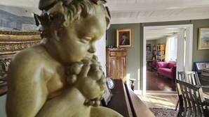 A room with a wooden statue, a desk, a bookshelf, and a pink sofa.