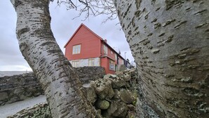 A red house with a stone wall and a large tree in the foreground.