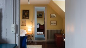 A room with a bed, a desk, a chair, a radiator, and a door leading to another room.