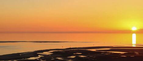 A sunset over a calm body of water with a beach in the foreground.