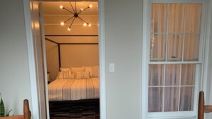 A bedroom with a bed, a ceiling light fixture, a window with curtains, and a wooden floor. - Beautiful S. Main St. Historic Row House (Geneva)