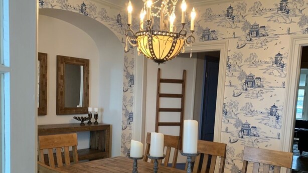 A dining area with a wooden table, chairs, a chandelier, and wallpaper with a blue and white pattern. - Beautiful S. Main St. Historic Row House (Geneva)