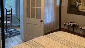 A bedroom with a large bed, a door leading to a balcony, a painting on the wall, and a small table with a chair. - Beautiful S. Main St. Historic Row House (Geneva)