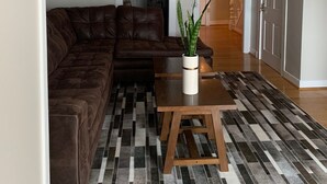 A modern living room with a sectional sofa, a coffee table, and a patterned rug. - Beautiful S. Main St. Historic Row House (Geneva)
