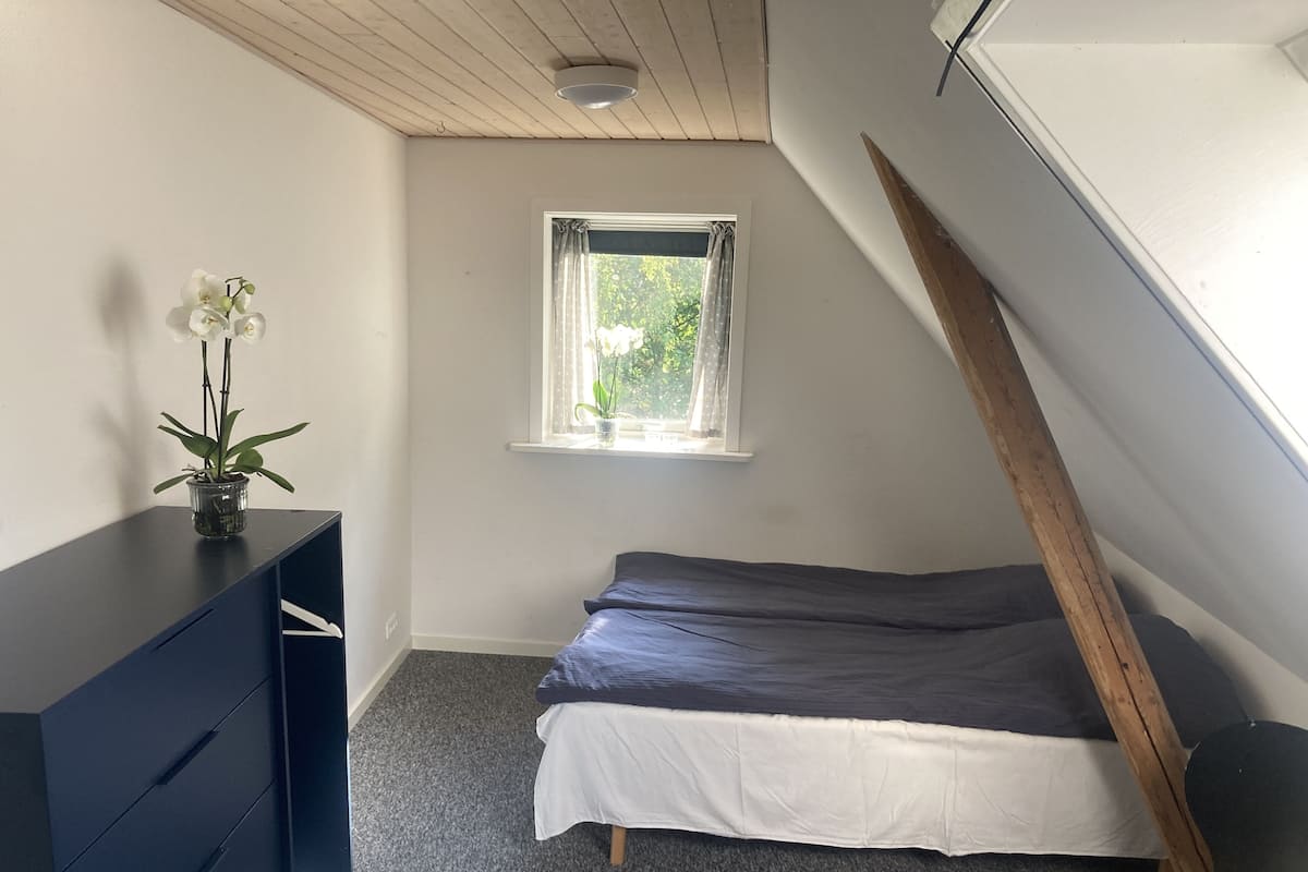 A bedroom with a bed, a dresser, a window with curtains, and a ceiling light.