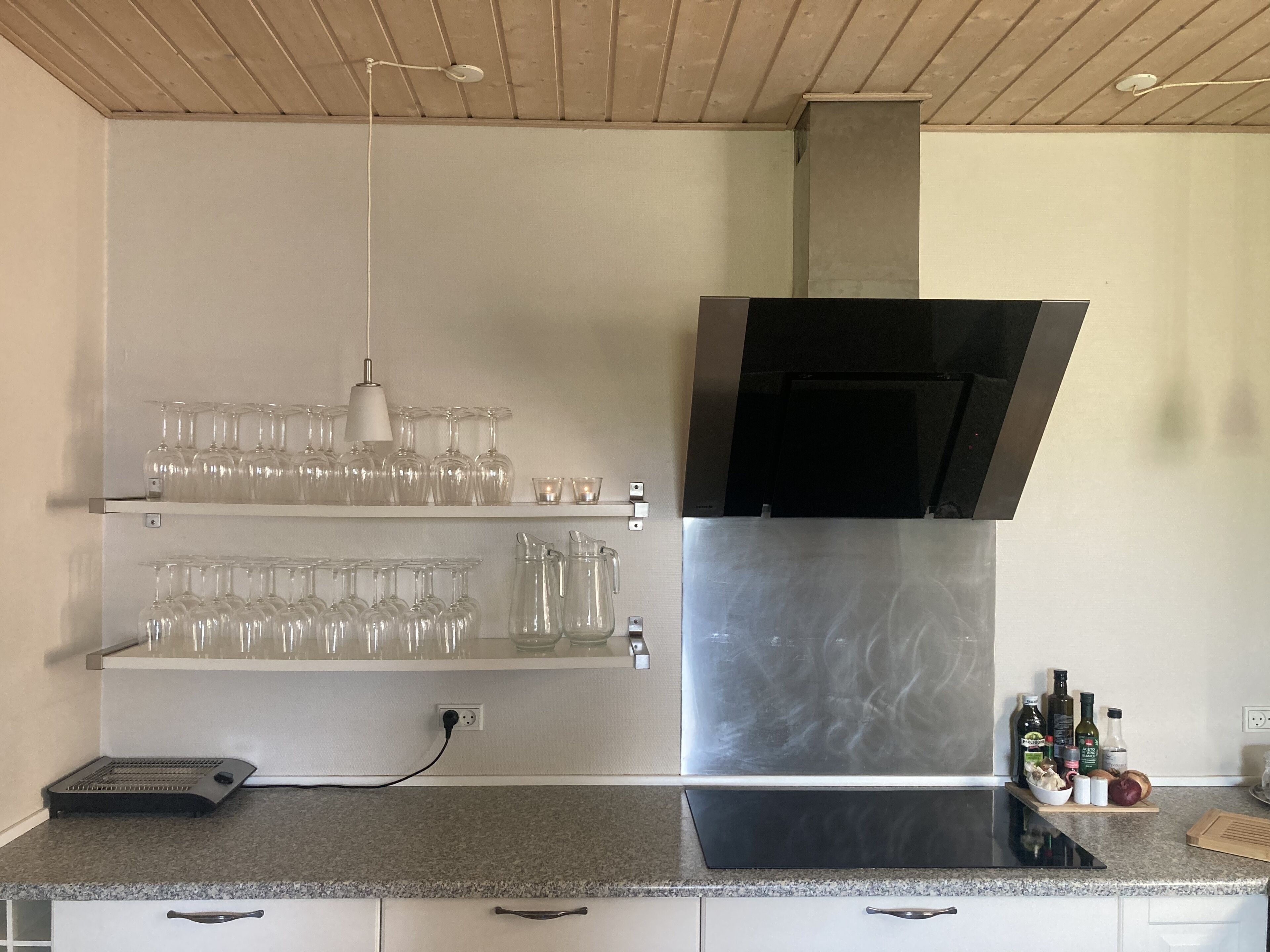 A kitchen with a stainless steel range hood, a countertop with a toaster, and shelves holding glassware.