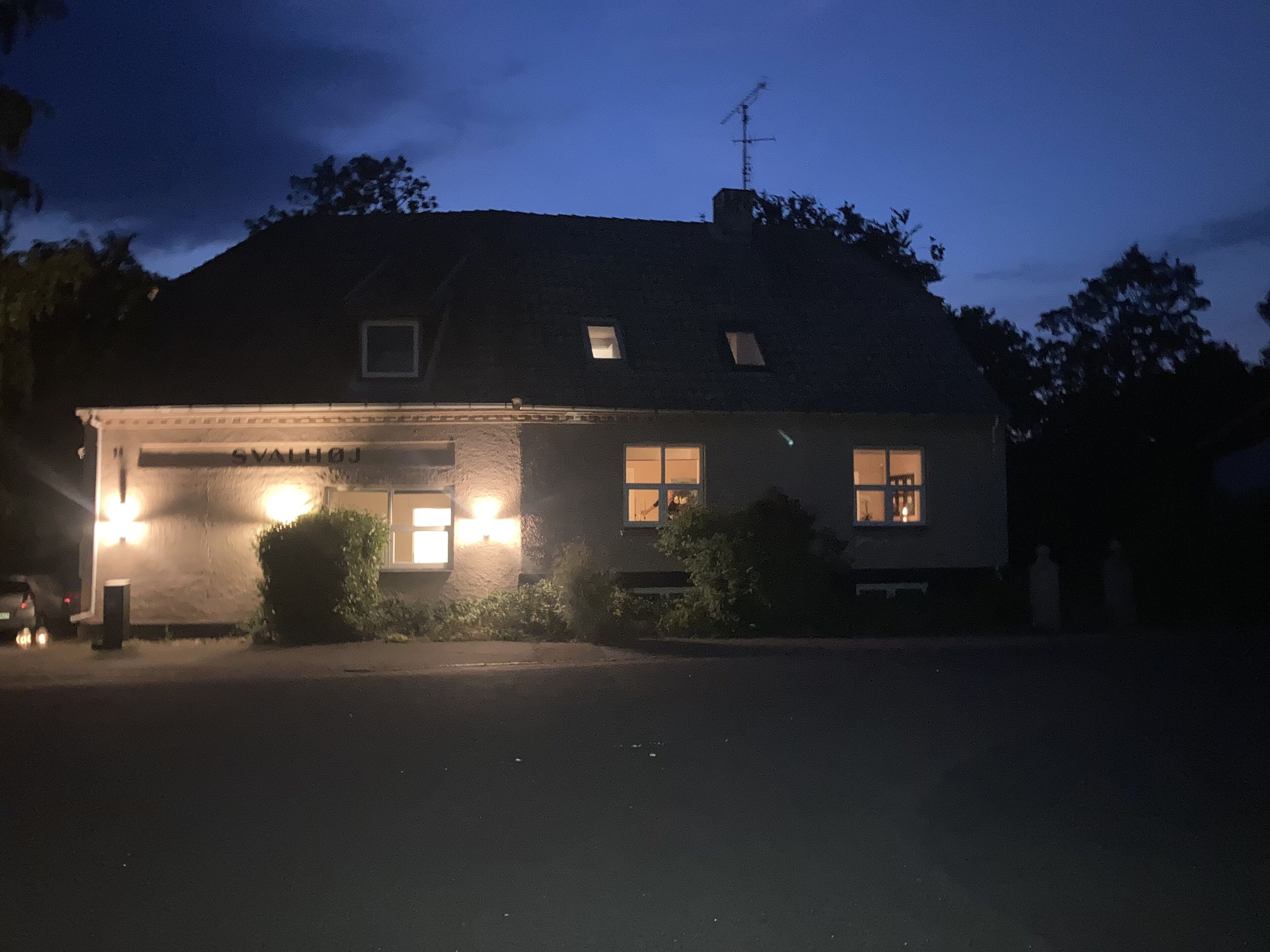 En byggnad med ett garage, en skylt med texten ”SVALHOFJ” och en skorsten.