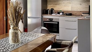 Une cuisine moderne équipée d’un réfrigérateur en acier inoxydable, d’un four et d’une machine à café posée sur le plan de travail. On peut voir un vase contenant des plantes séchées sur la table.