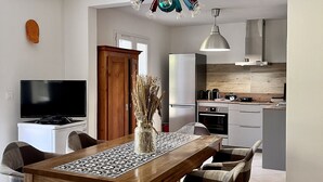 Une cuisine moderne dotée d’un four encastré, un coin repas avec une table et des chaises en bois, et un téléviseur fixé au mur.