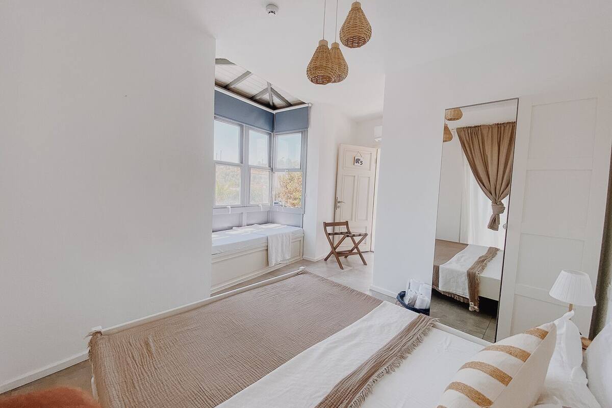 Une chambre avec un grand lit, un coin fenêtre aménagé en siège, une chaise et un miroir.