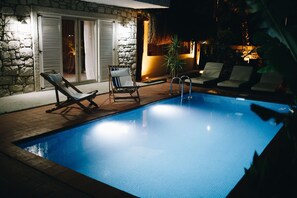 A swimming pool with two lounge chairs and a small table, surrounded by stone walls and a thatched roof structure. - Dud Otel Alaçatı (Cesme)