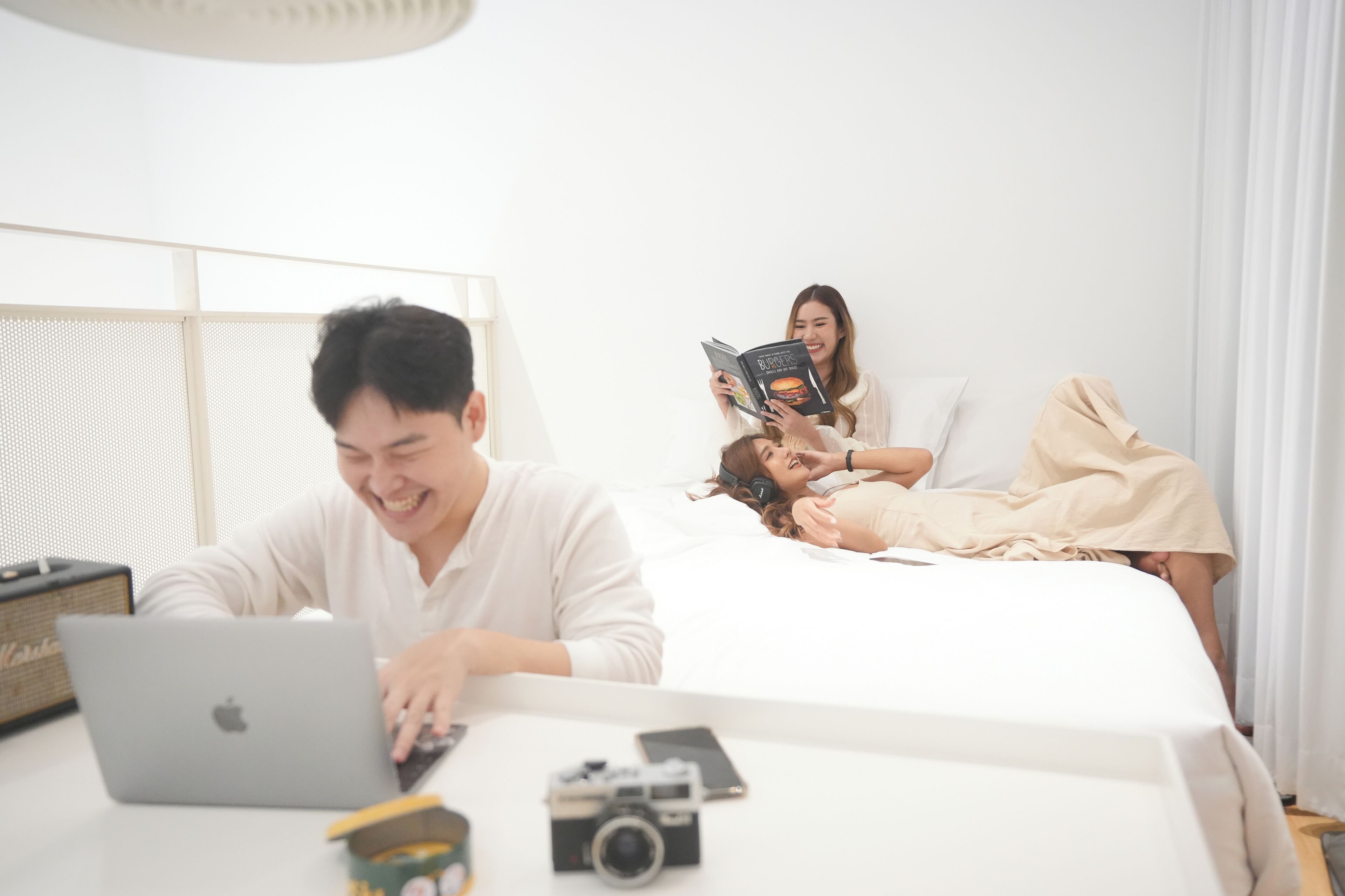 A modern hotel room with a bed, a laptop, and a person using a smartphone.