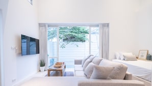 Una habitación moderna y luminosa, con un ventanal grande, un sofá, una cama y un televisor de pantalla plana en la pared.