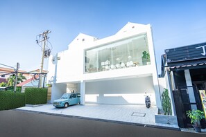 Um edifício moderno com fachada de vidro, área de estacionamento e um pequeno jardim.