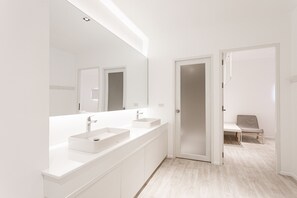 Uma casa de banho moderna com um espelho grande, duas bacias e uma cadeira no quarto vizinho.